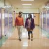 Two people walk down a school hallway wearing masks
