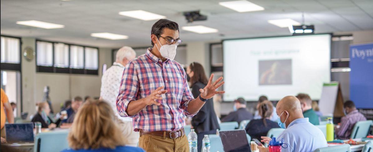 A person wearing a mask speaking in a room with other people