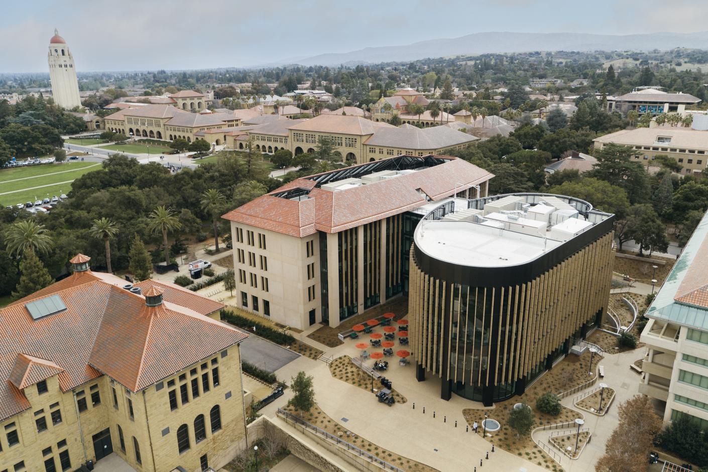An aerial view of a university campus featuring modern architecture, lush greenery, and a prominent clock tower in the background.