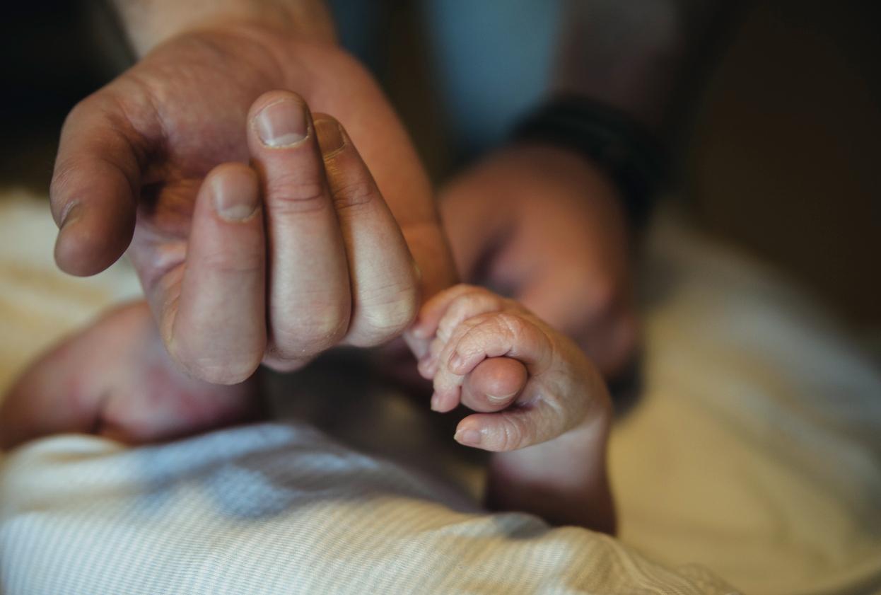 Newborn baby holding the pinky finger of a parent