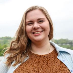 Image of female with blonde hair wearing a brown sweater and blue shirt.