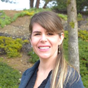 Image of blond woman wearing a blue blazer, standing in front of greenery.