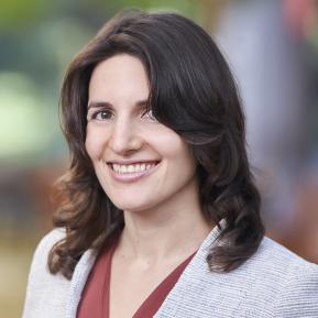 Image of female with brown hair wearing a grey suit and brown top