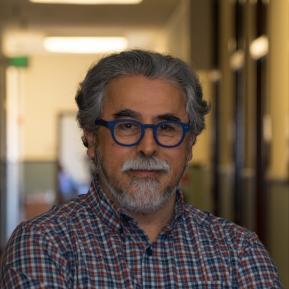 Image of male with beard and mustache wearing blue glasses and checked shirt.