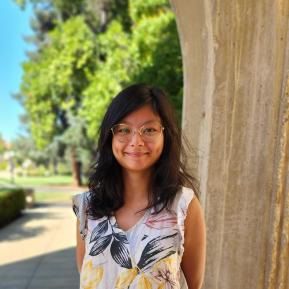 Asian female wearing a white dress with colorful leaves, standing in front of greenery