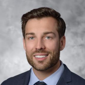 Image of male with brown hair wearing a black suit and blue shirt