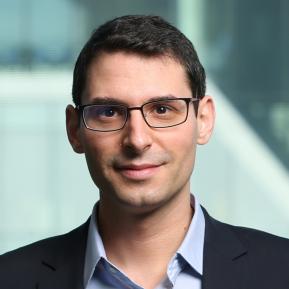 Image of male with black hair and glasses wearing a black suit and blue shirt