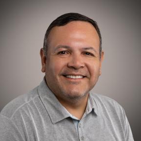 A person is wearing a light gray polo shirt with a collar and buttons. The background is a soft gradient, transitioning from dark to light, creating a professional-looking backdrop. The lighting highlights the texture of the shirt, giving a clean and polished appearance.