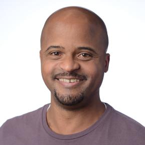 A person is wearing a casual, short-sleeved, deep purple t-shirt. They are positioned against a solid white background, giving a clean and simple appearance. The lighting is soft, emphasizing the relaxed nature of the attire.