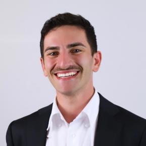 A person is dressed in a formal black suit jacket over a white dress shirt. The background is a clean, light color, emphasizing the professionalism of the attire, suitable for a business setting or portrait.