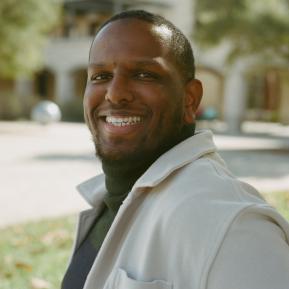 male wearing a green top and white jacket