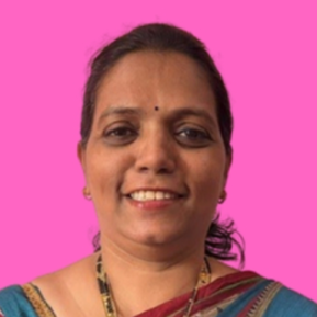 A woman is smiling at the camera, wearing a colorful traditional saree in shades of blue and red. She has a bindi on her forehead and earrings, and her hair is tied back. The background is a vibrant pink, making her image stand out.
