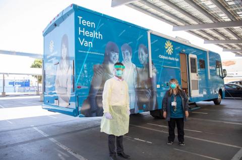 Two people stand in front of the Teen Health Van wearing personal protective equipment
