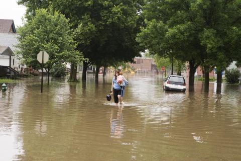 A woman carrying a baby through a flooded street