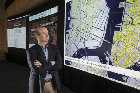  Communication Professor Jay Hamilton in front of a large data visualization showing taxi pickups in New York during Hurricane Irene compared to one week before