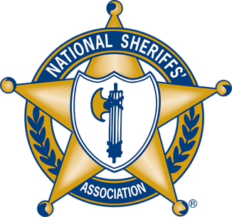 The image shows the logo of the National Sheriffs' Association. It features a gold sheriff's star, with a central emblem that includes a blue and white shield. The text "NATIONAL SHERIFFS' ASSOCIATION" curves along the top of the star, and there are decorative elements, including laurel branches, surrounding the star.