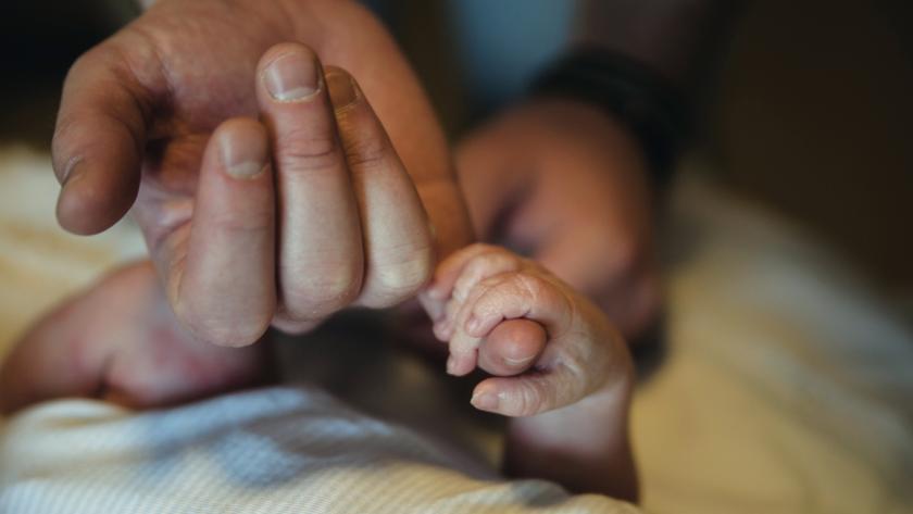 Newborn baby holding the pinky finger of a parent