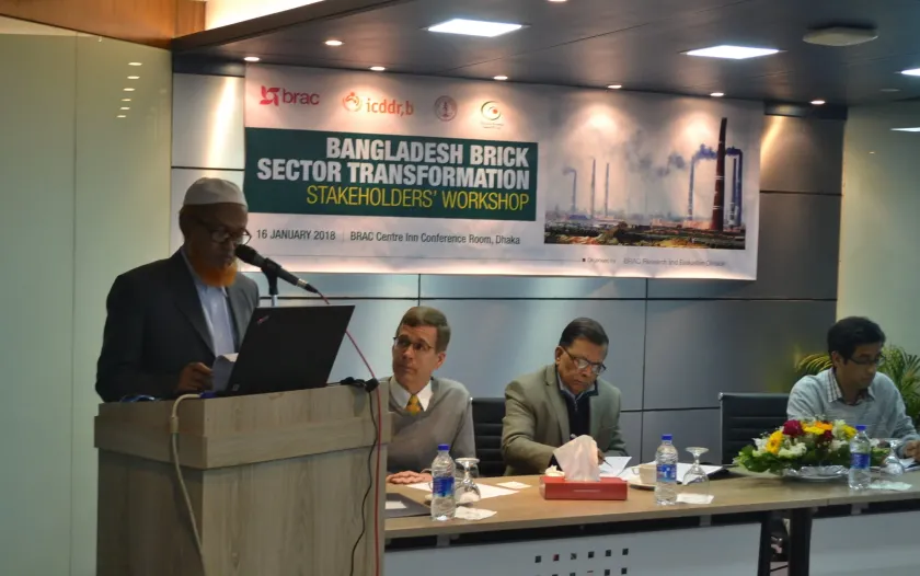 Jamil Hussain, vice president of Bangladesh's national brick manufacturing association, speaks at the podium during a 2018 meeting. Stephen Luby is seated to his left.