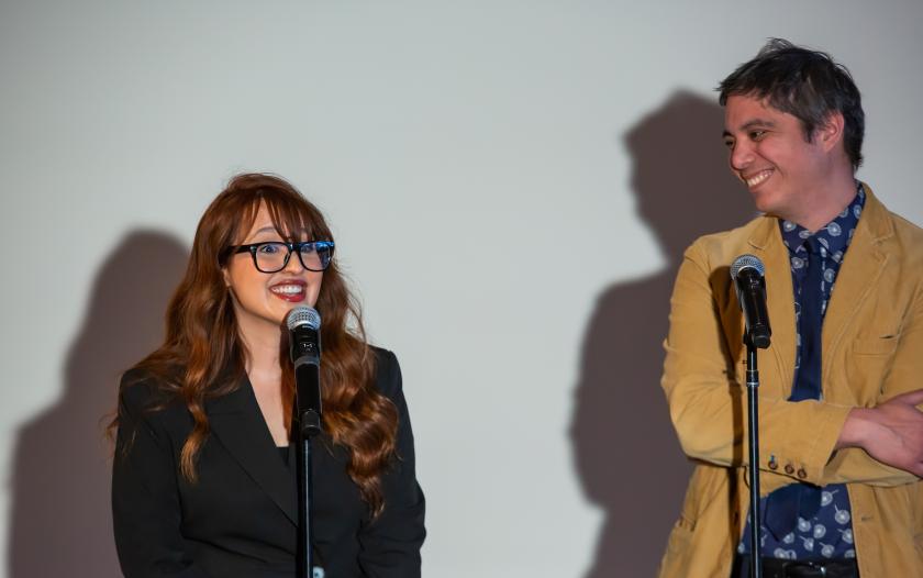 image of female speaking on a mic, and a male standing next to her with smiling with a mic