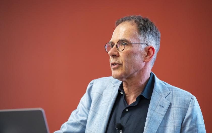 Man wearing a blue suit jacket and black shirt with glasses.