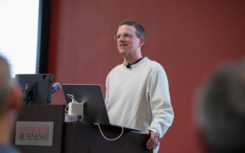 man standing in front of podium wearing a white sweater